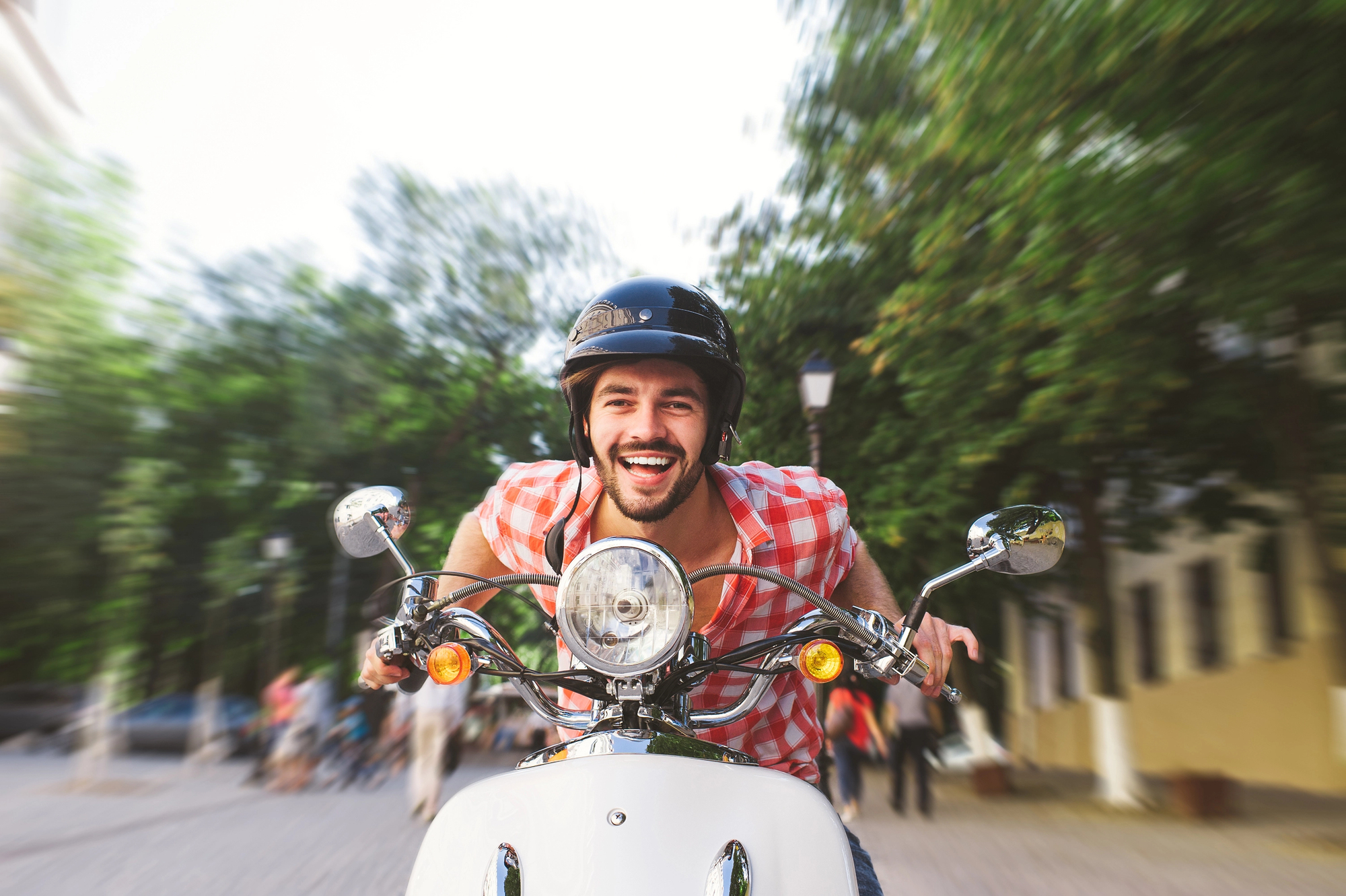 Man riding electric scooter on city street wearing helmet, highlighting debate over whether e-bikes should be licensed like motor vehicles in Ontario.