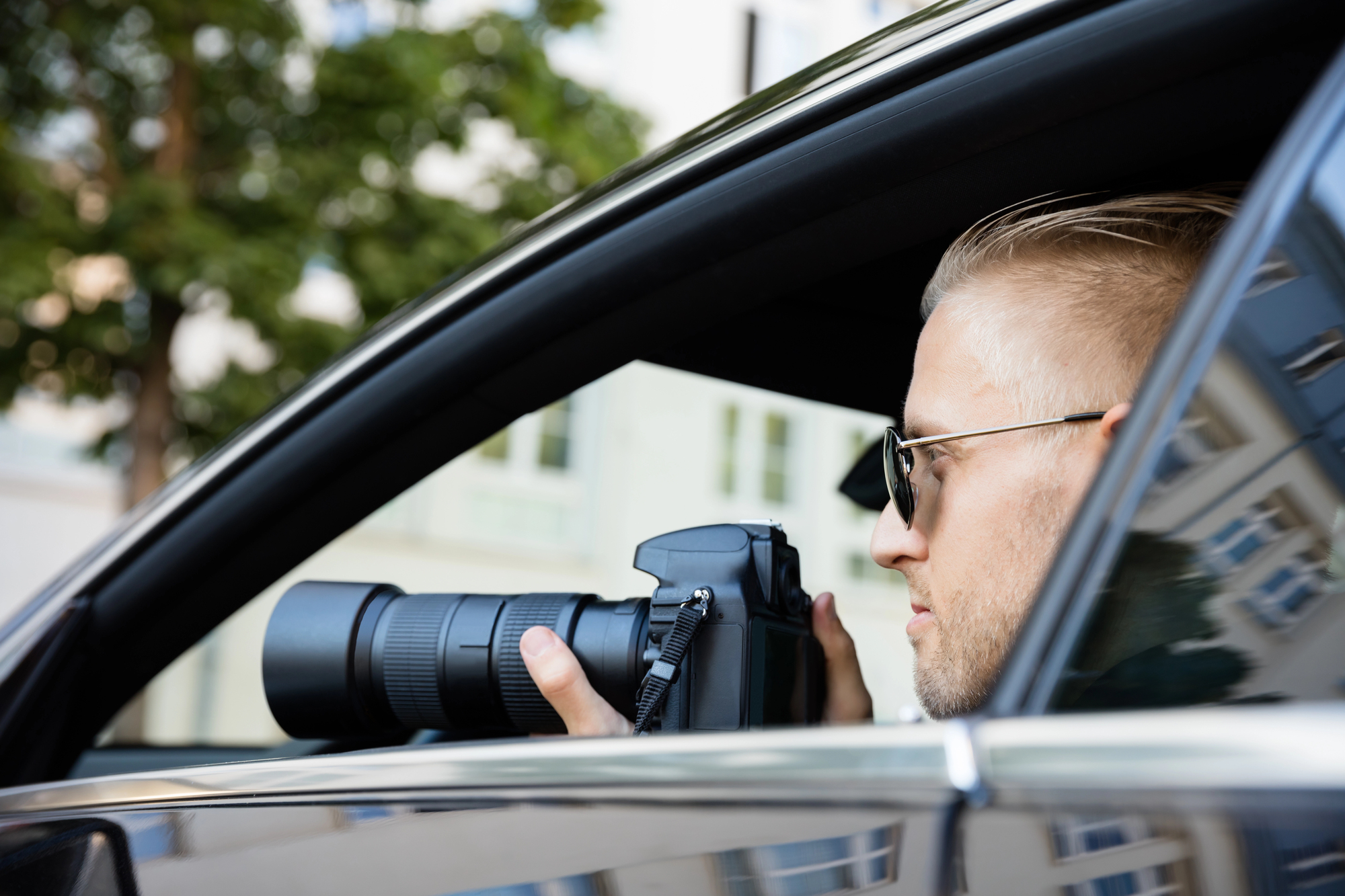 Private investigator using a camera from inside a vehicle to conduct disability surveillance for an insurance claim investigation.
